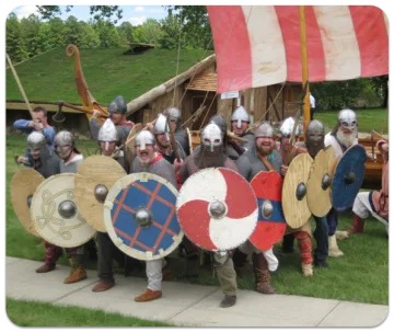 Vikings posing with shields in front of a longhouse