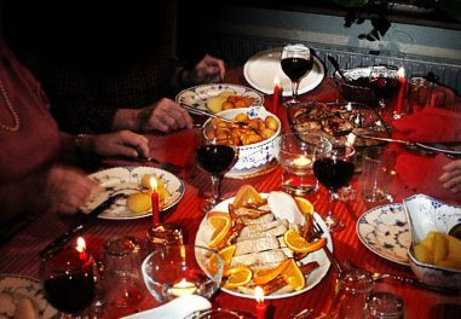 Candlelit Danish Christmas table with fish, potatoes, oranges, wine, and red heart decorations.