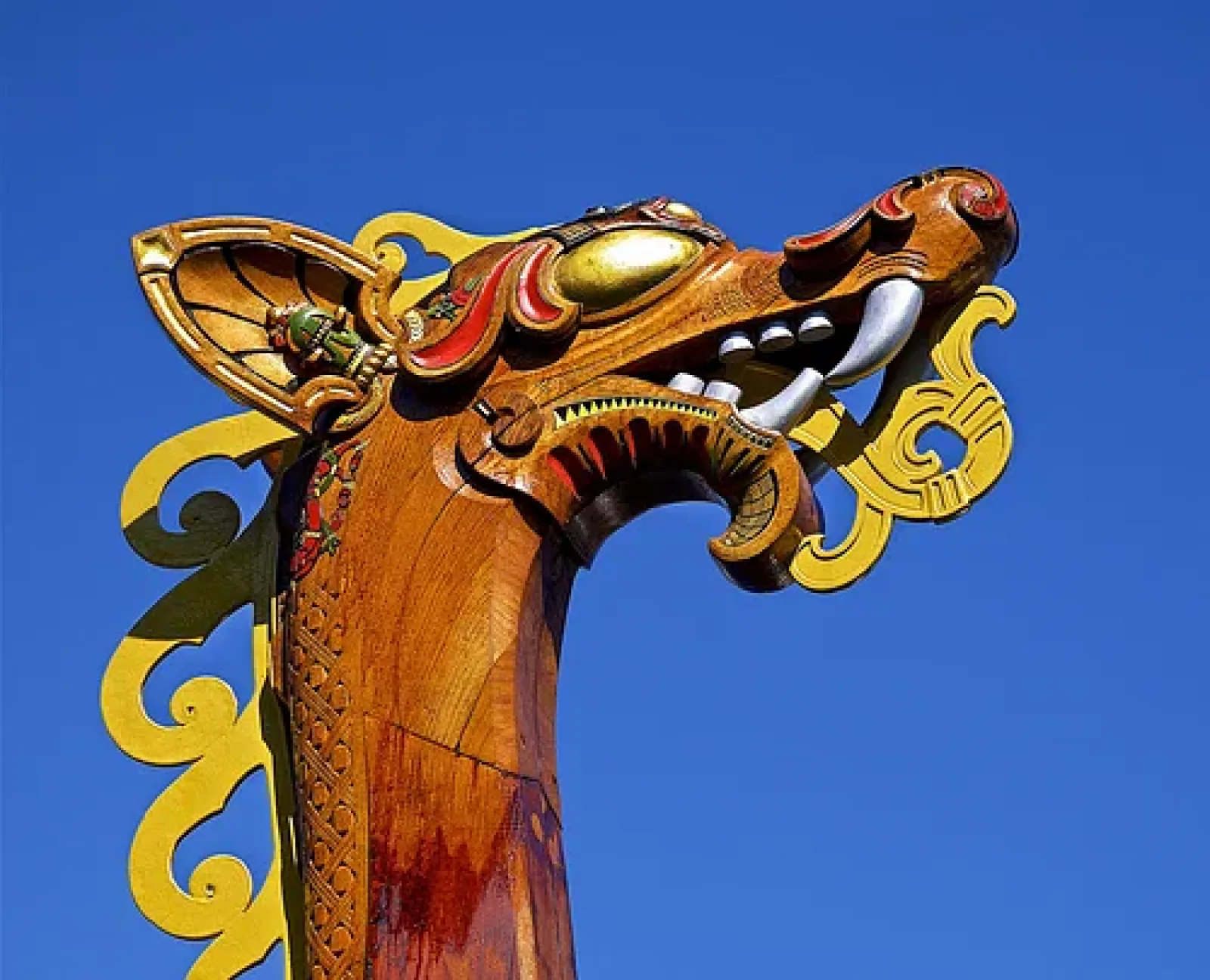 Colorful carved dragon head detail on a Viking-style ship prow against blue sky.