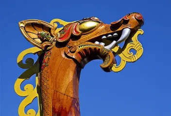 Colorful carved dragon head detail on a Viking-style ship prow against blue sky.